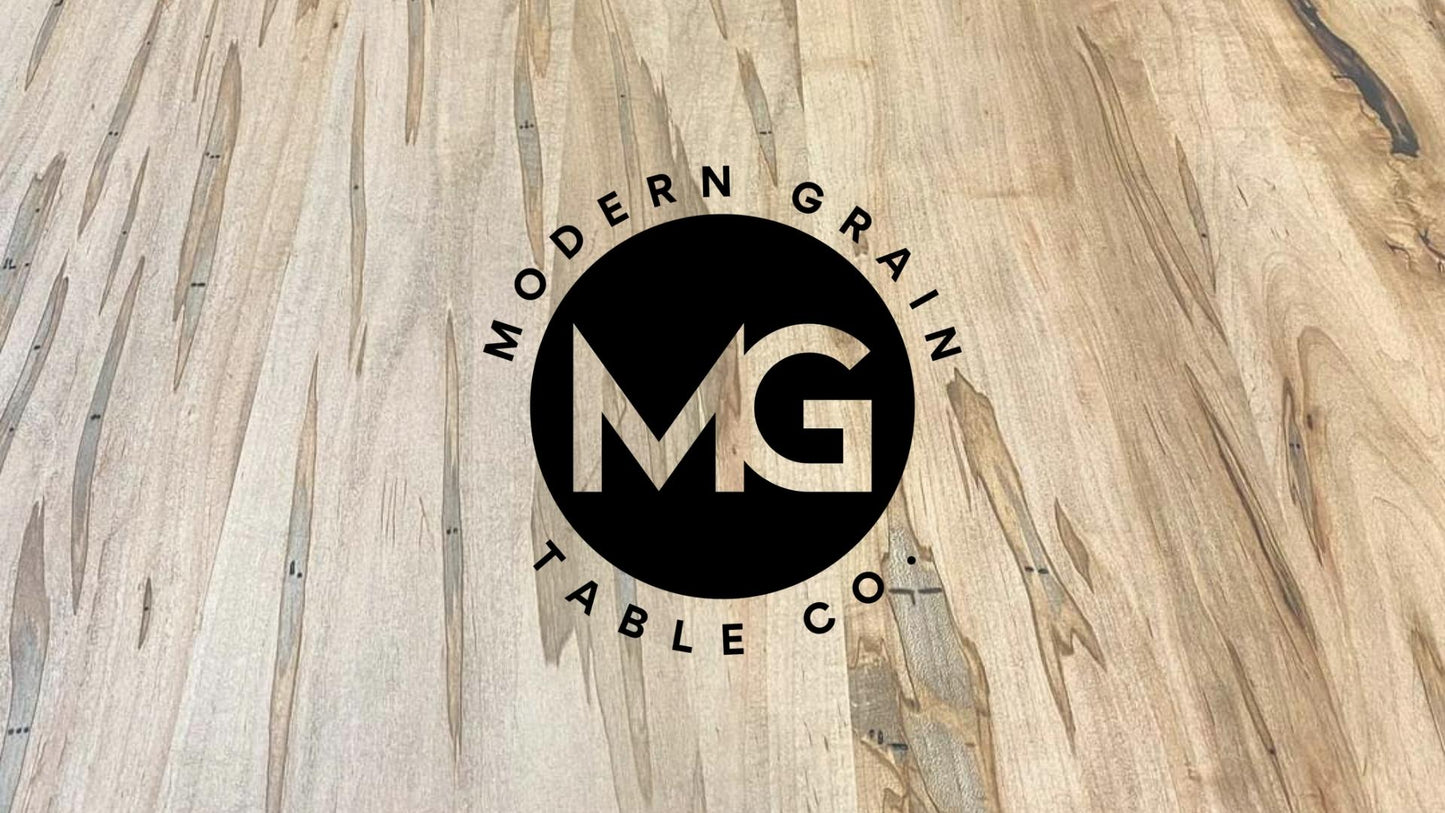 Modern Grain Table Co. logo over ambrosia maple hardwood grain background – handcrafted custom table brand based in Michigan