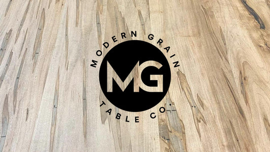 Modern Grain Table Co. logo over ambrosia maple hardwood grain background – handcrafted custom table brand based in Michigan